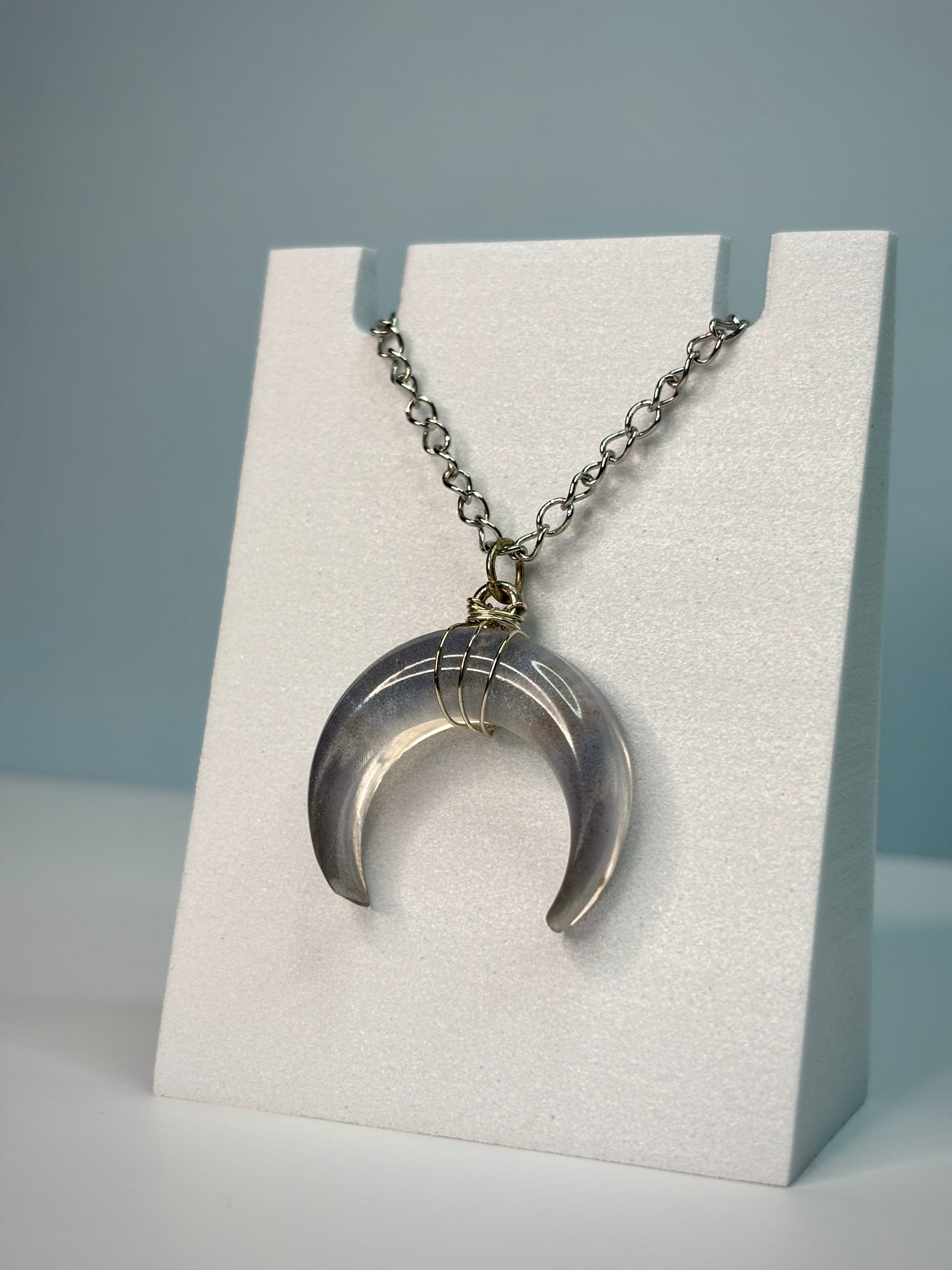 Silver crescent moon pendant on a chain displayed on a white card with a gray background