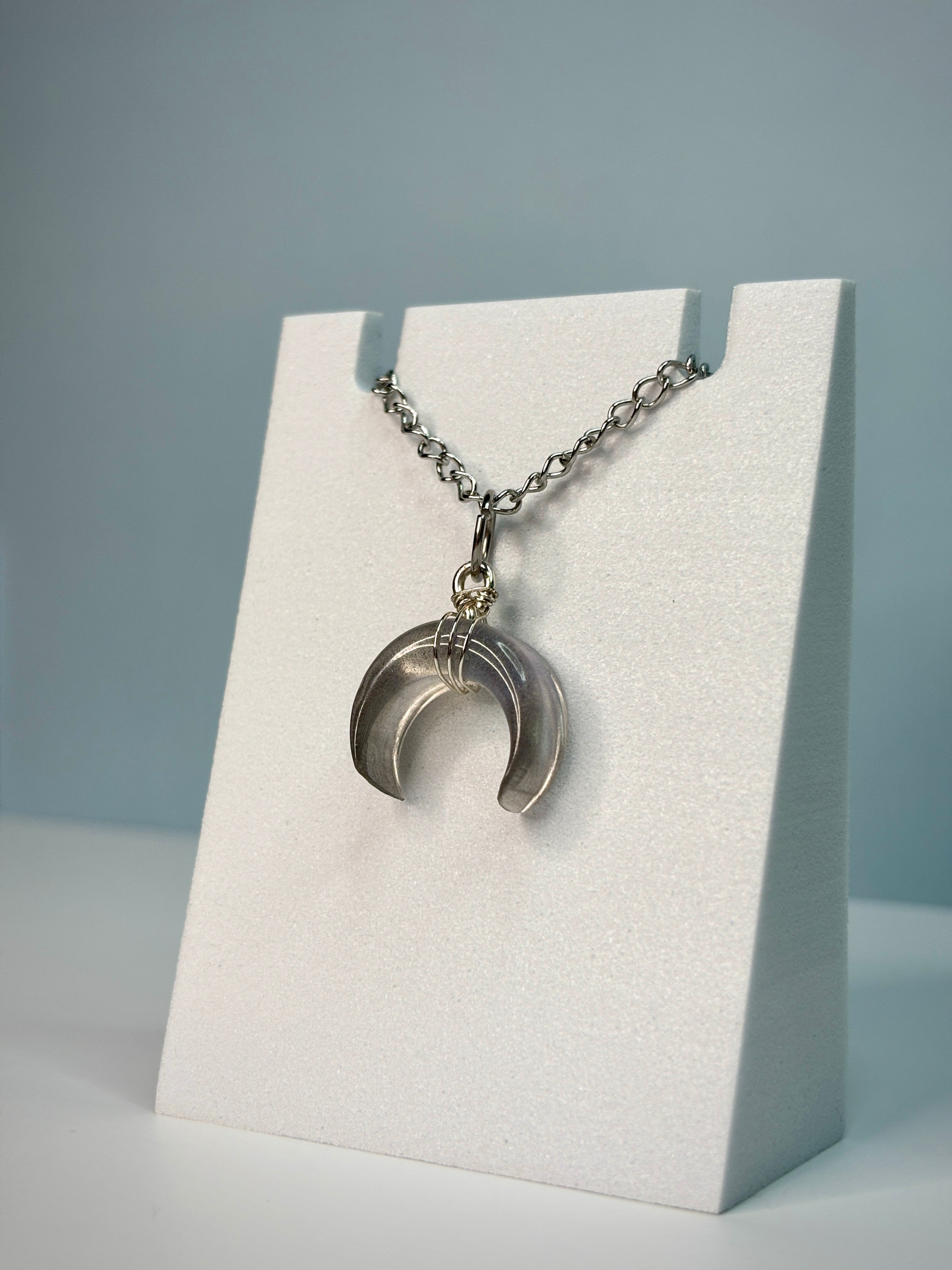 Silver crescent moon necklace on a white card with a gray background