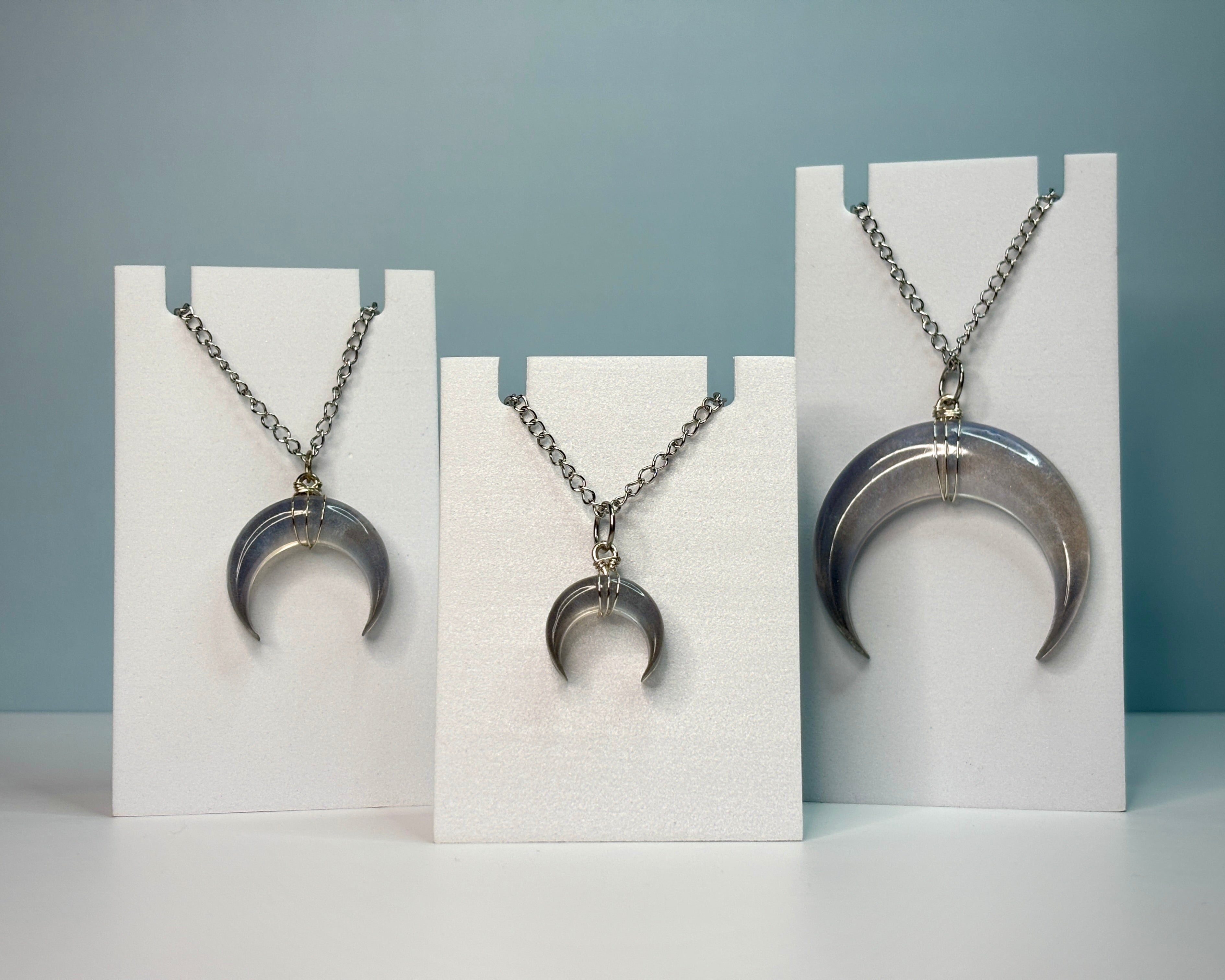 Three moon-shaped pendant necklaces on white stands against a gray background