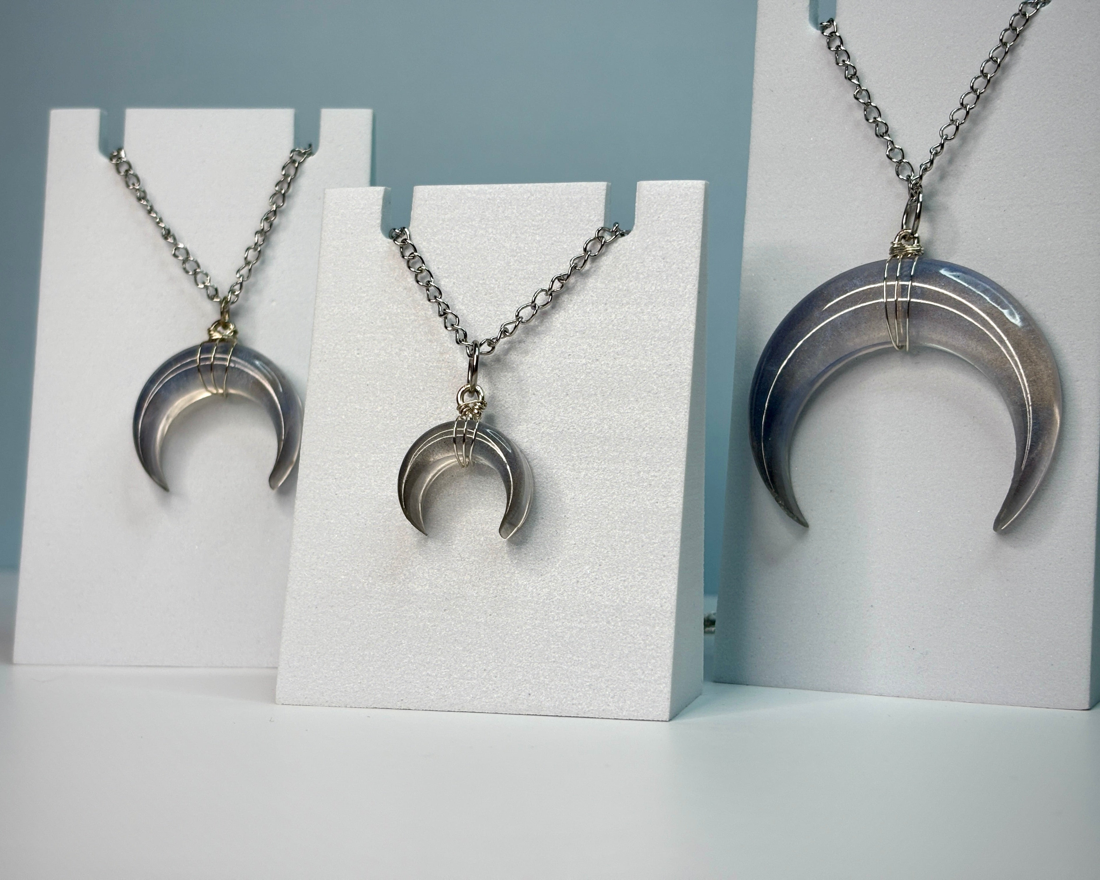 Silver crescent moon necklace on a white stand against a gray background