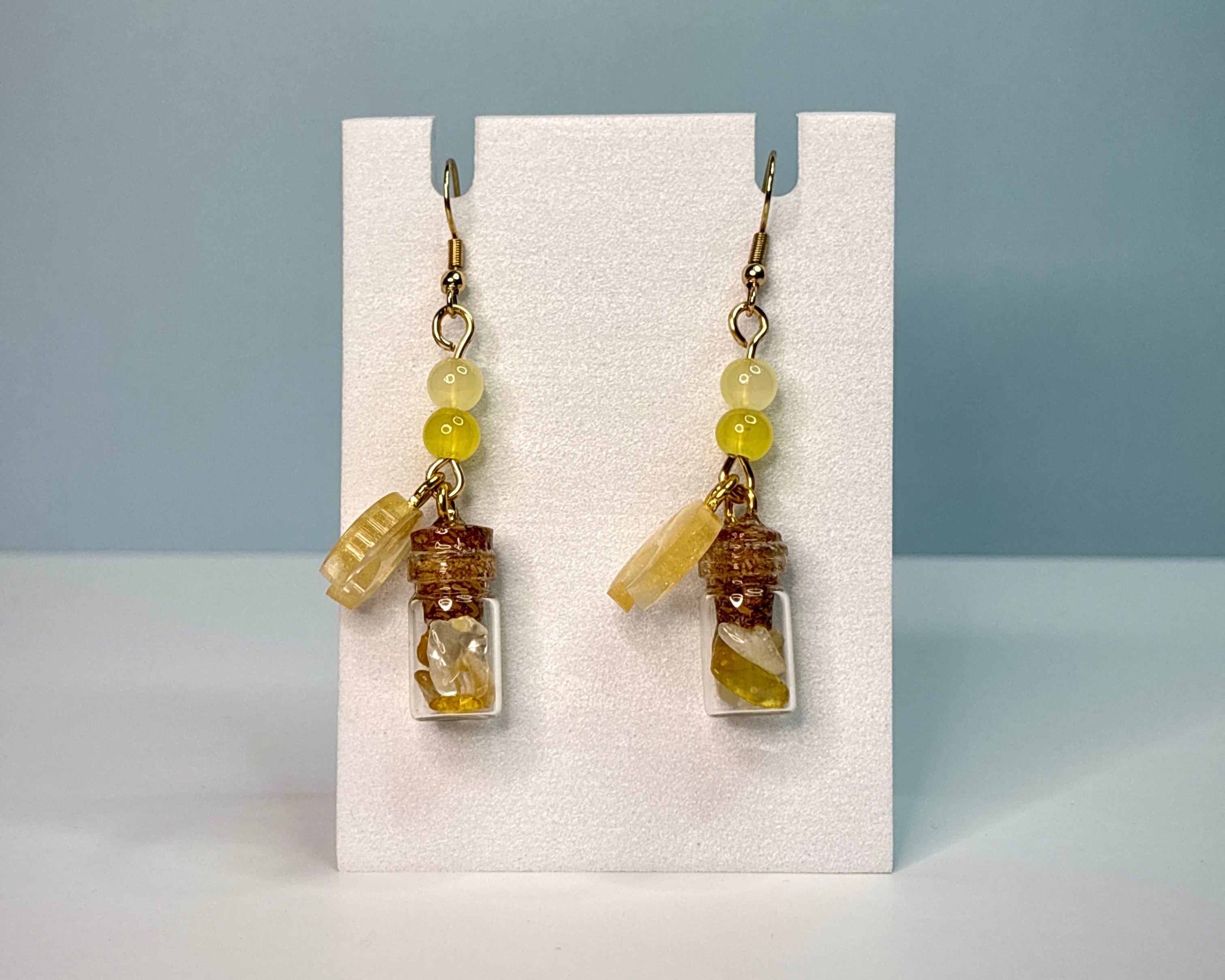 Pair of earrings with small bottles and beads on a white card against a blue background