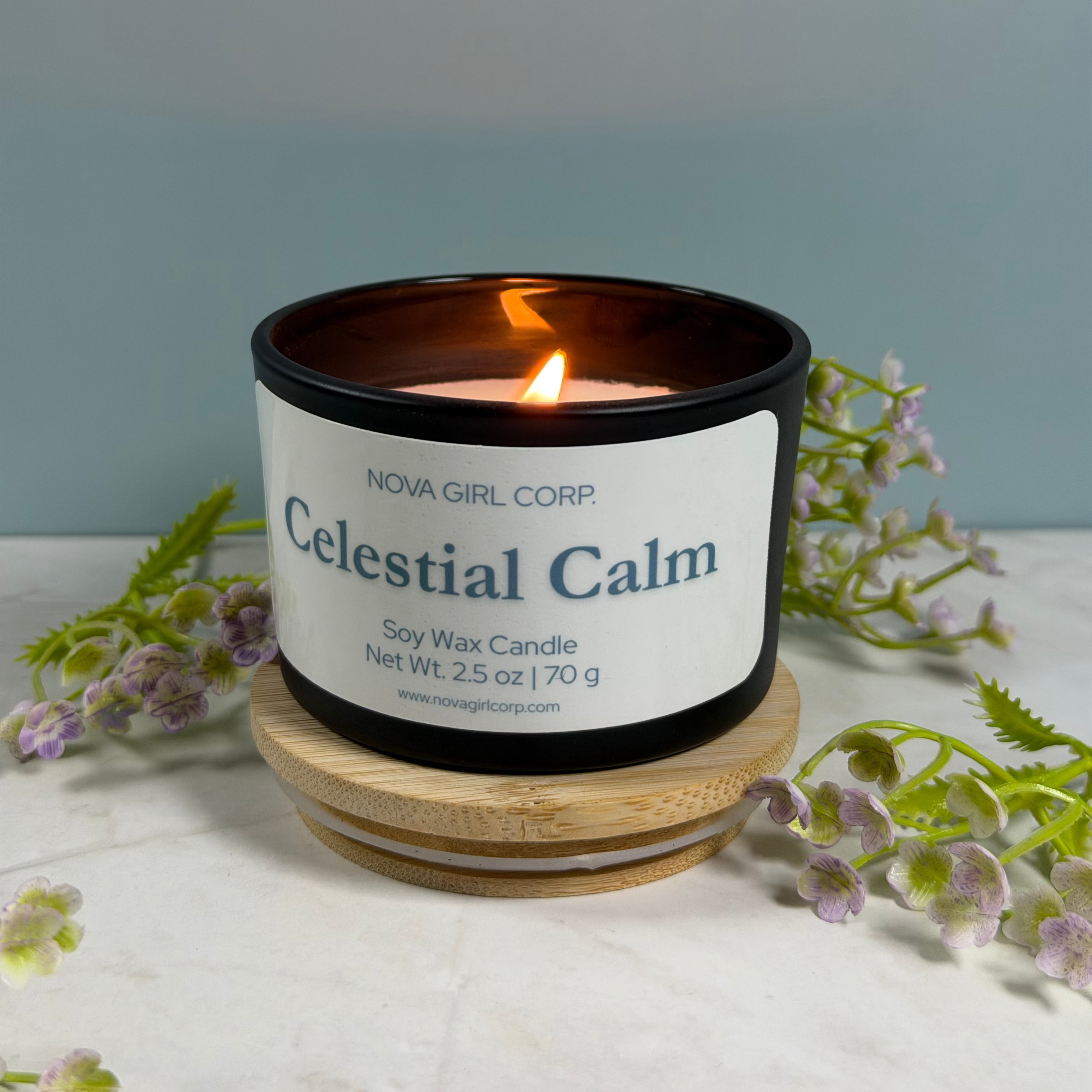 Candle labeled 'Celestial Calm' by Nova Girl Corp on a white surface with flowers.