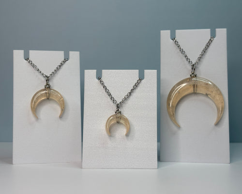 Three crescent moon-shaped pendants on necklaces displayed on white stands against a gray background.