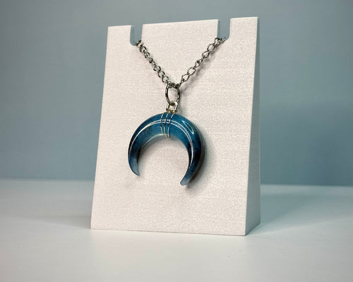 Blue crescent moon necklace on a white stand with a gray background