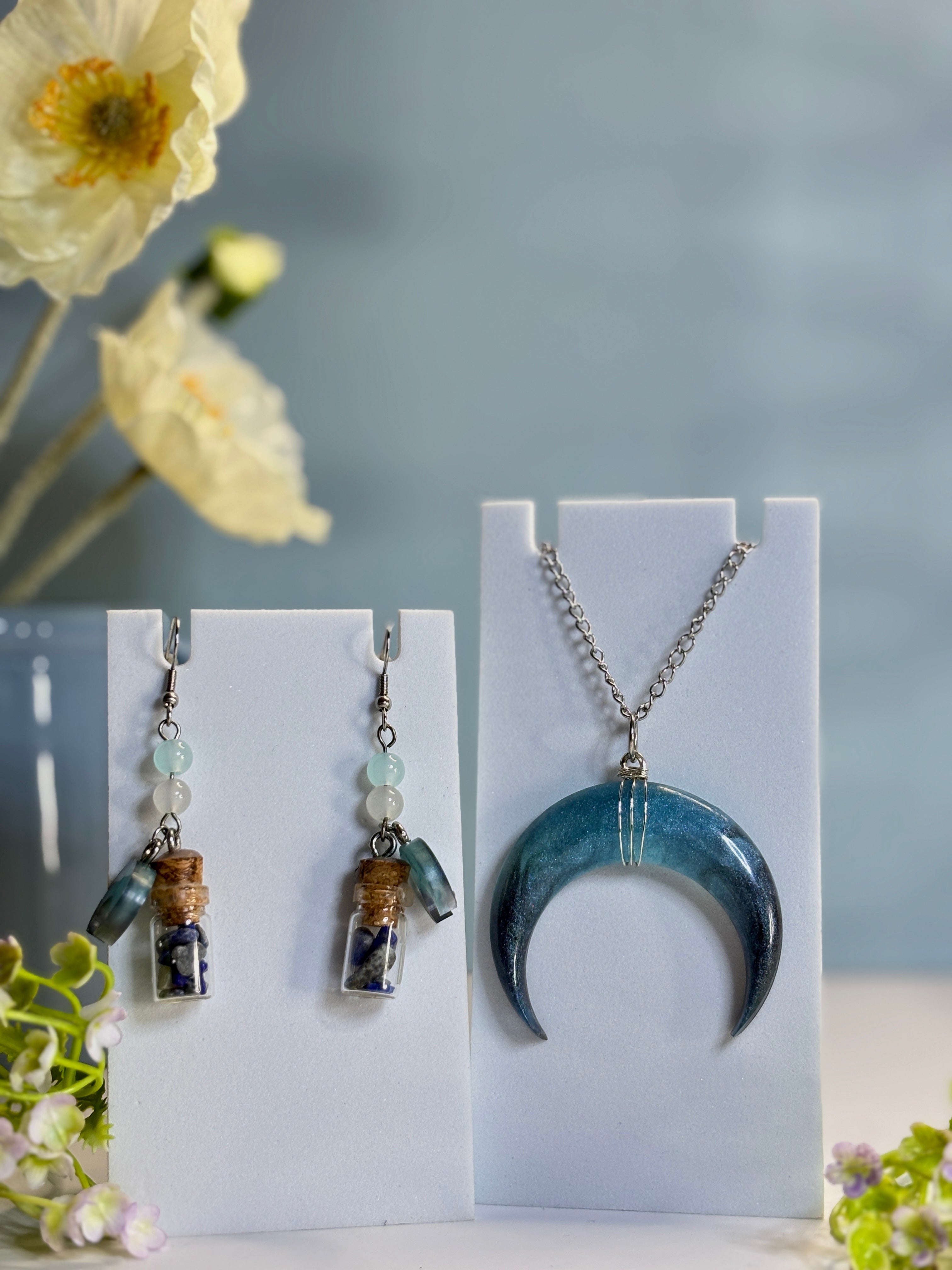 Jewelry set with necklace and earrings on display cards, surrounded by flowers.