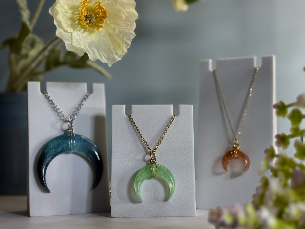 Three necklaces on display stands with flowers in the background