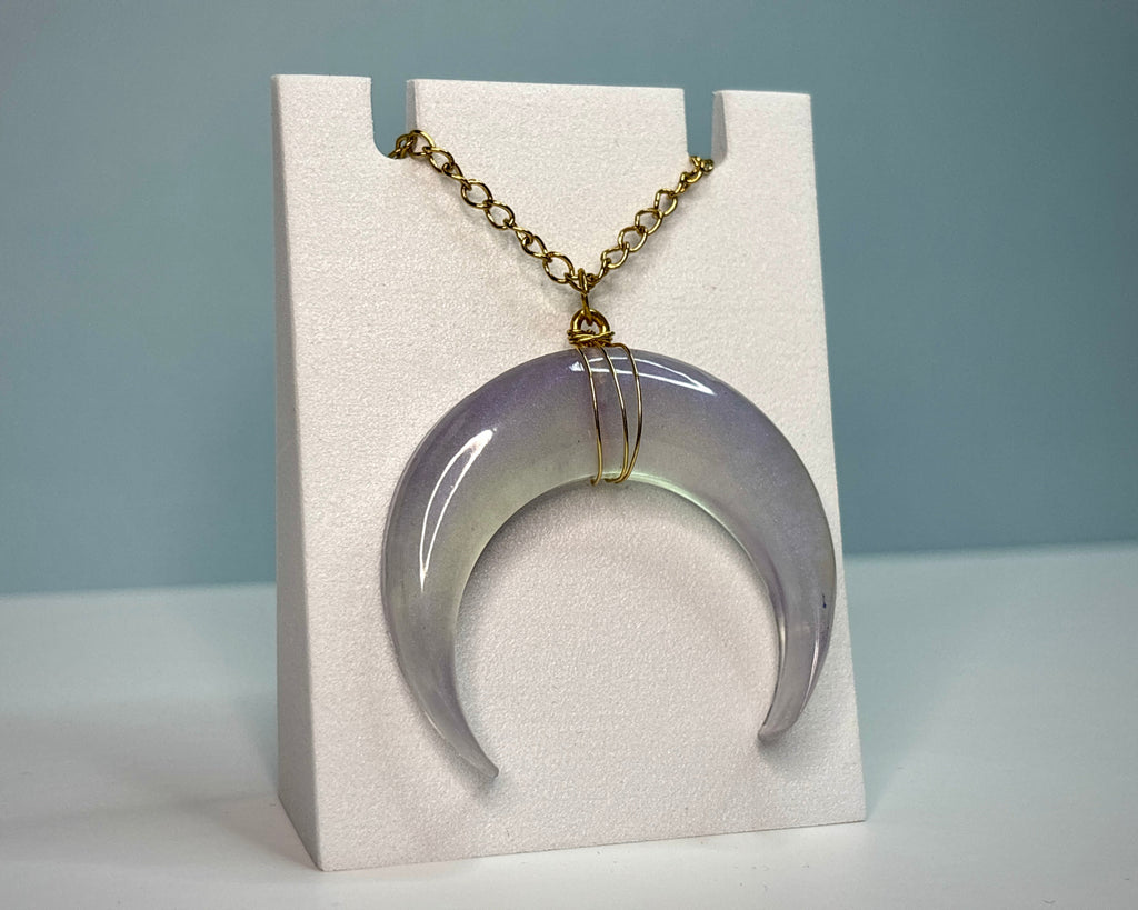 Necklace with a crescent moon-shaped pendant on a white stand against a light blue background