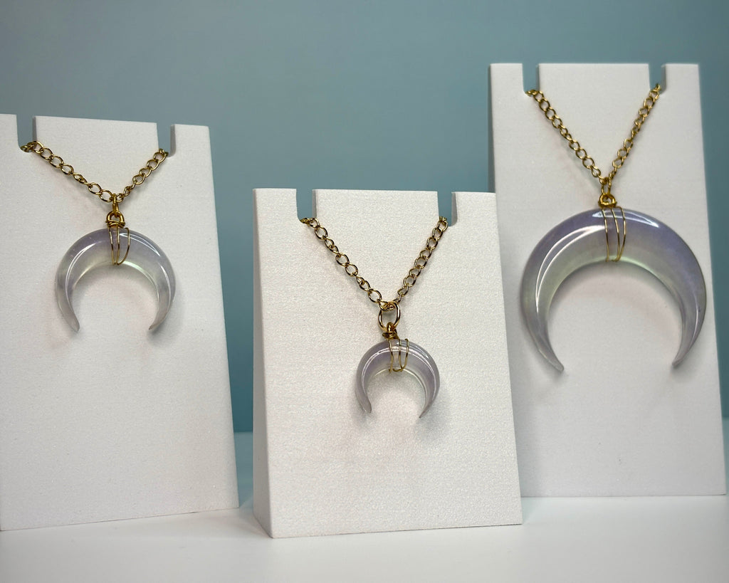 Three crescent moon pendants on white stands against a blue background