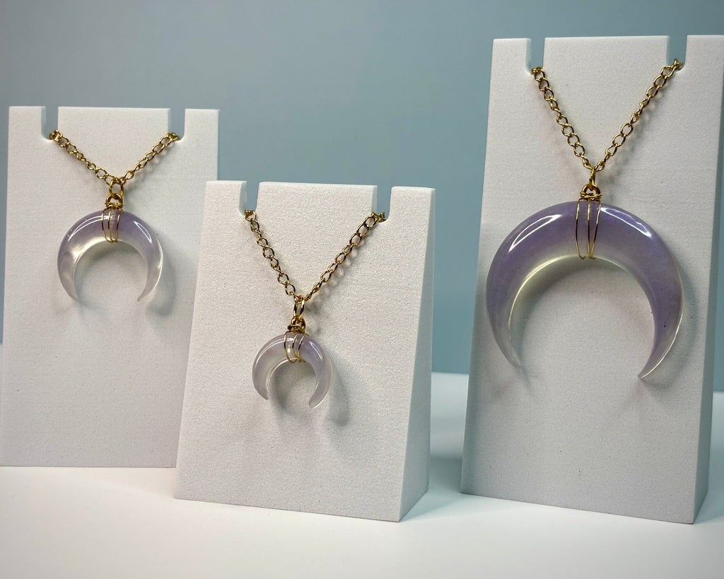 Three necklaces with purple crescent moon pendants on white card holders against a light blue background.