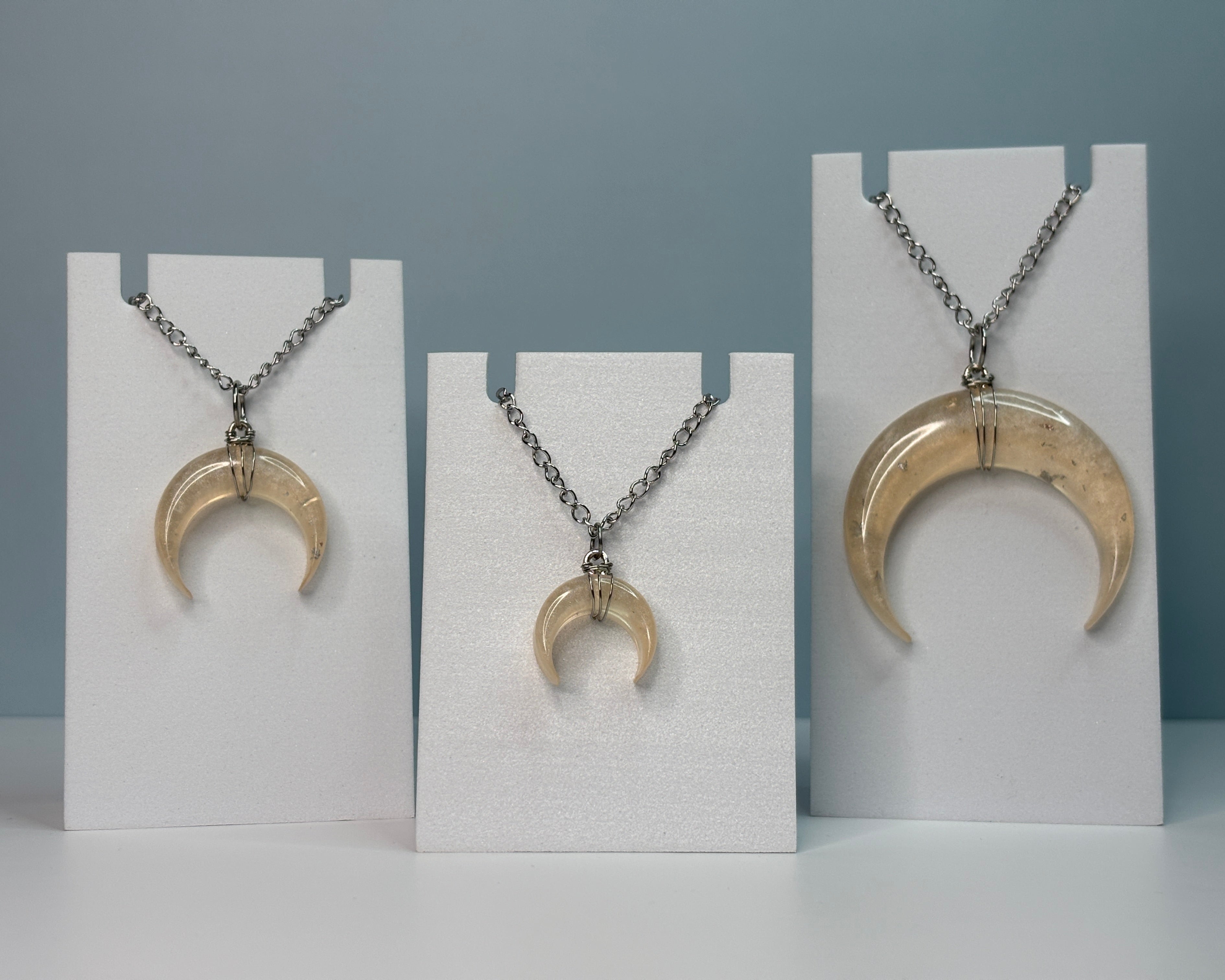 Three crescent moon-shaped pendants on necklaces displayed on white stands against a gray background.