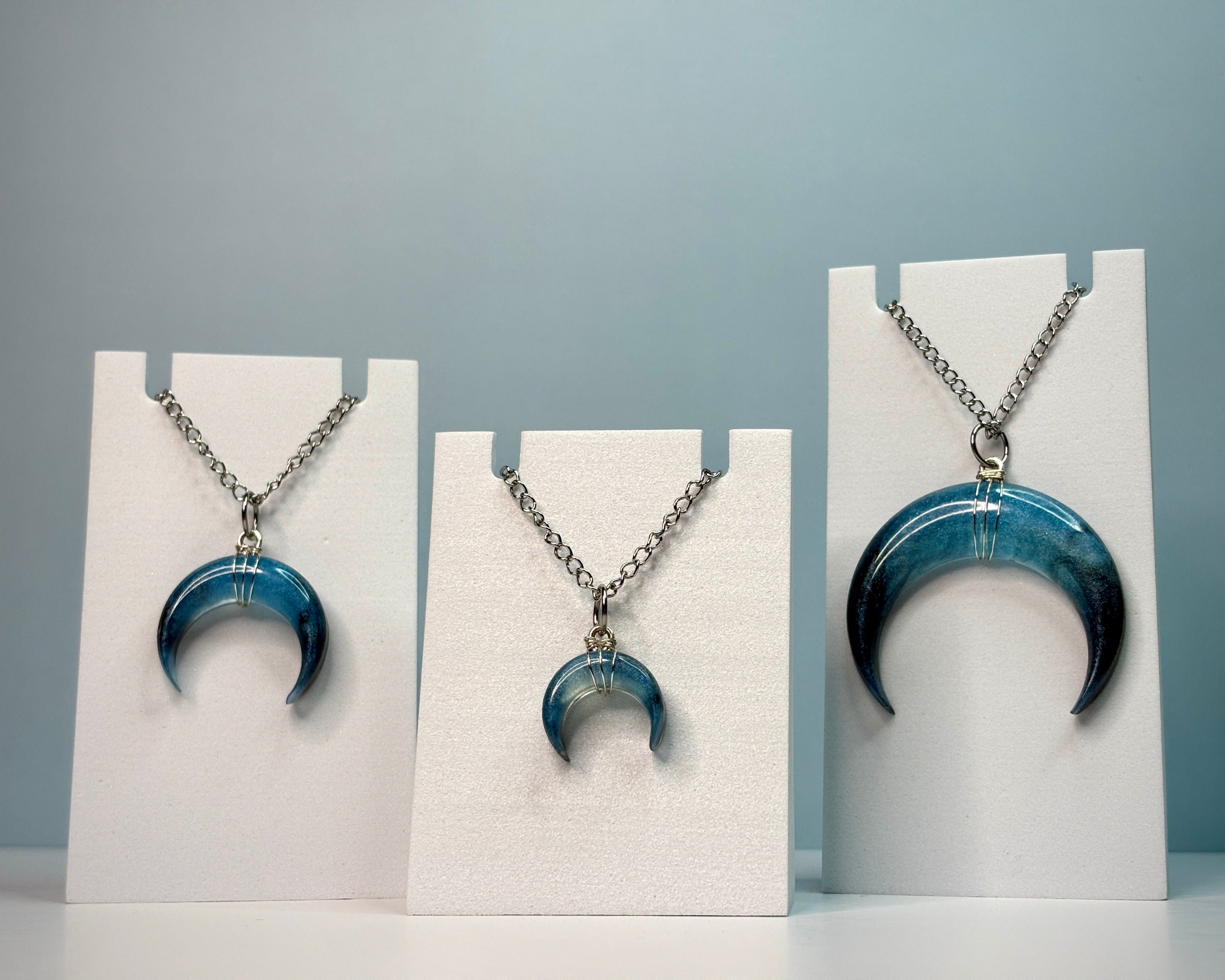 Blue crescent moon necklace on a white stand against a light blue background