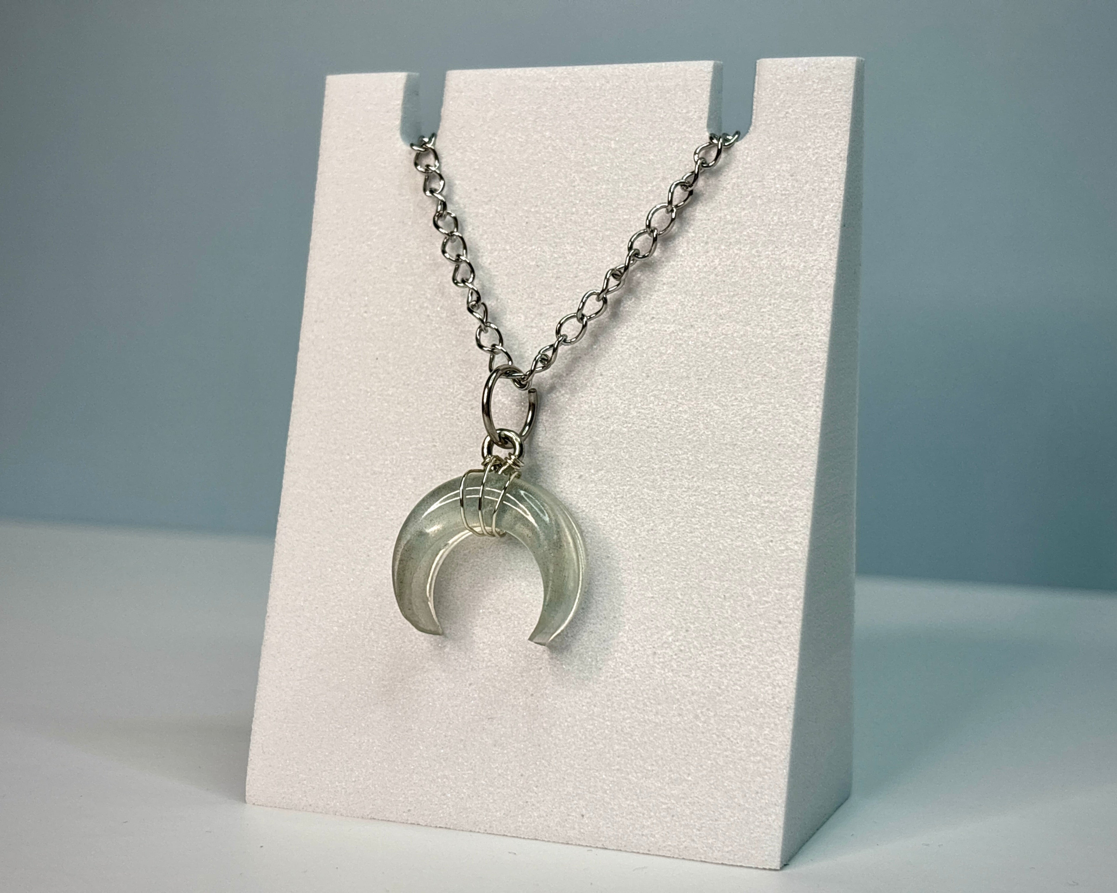 Necklace with a crescent moon pendant on a white stand against a gray background