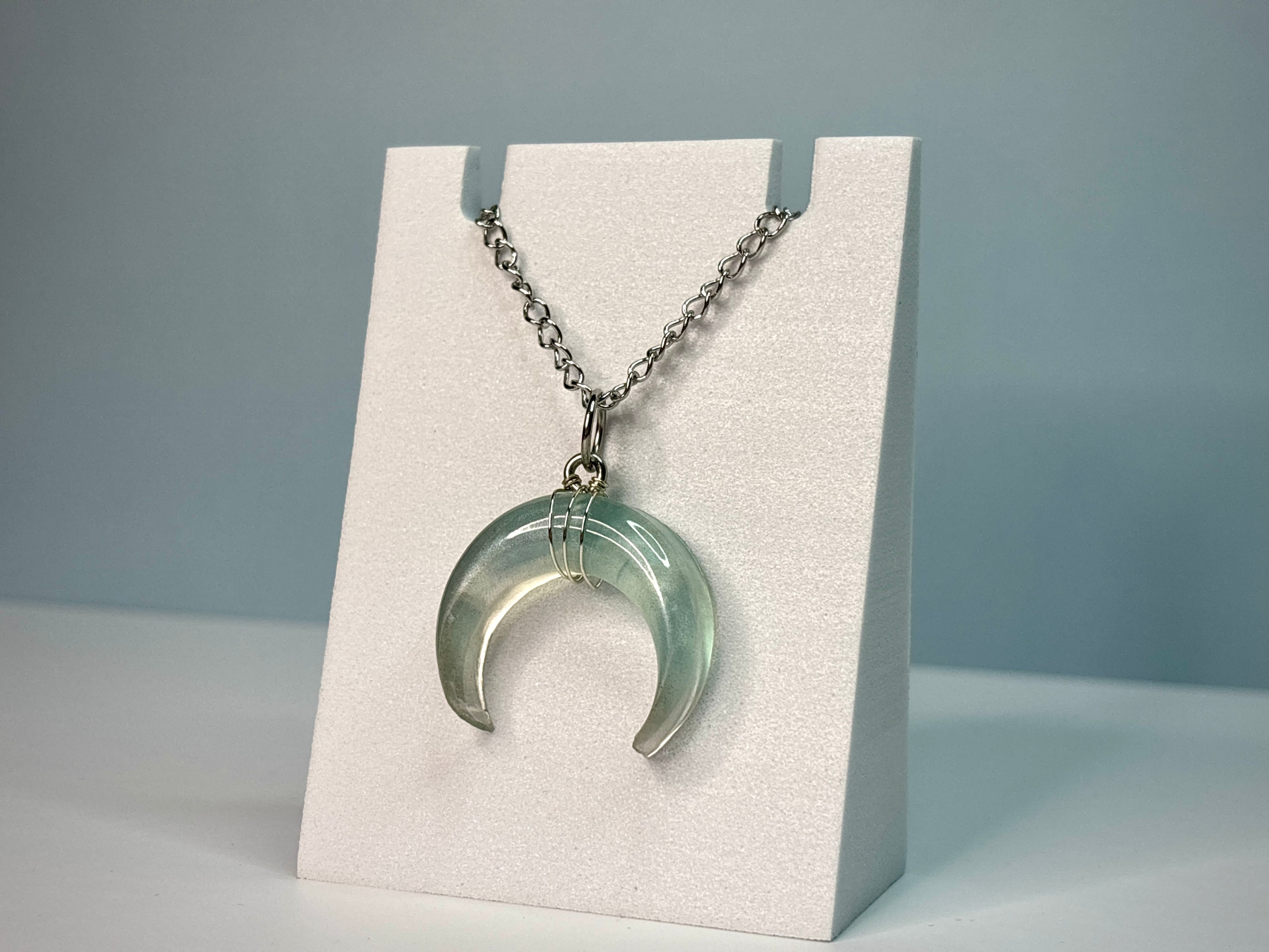 Necklace with a crescent moon pendant on a white stand against a gray background