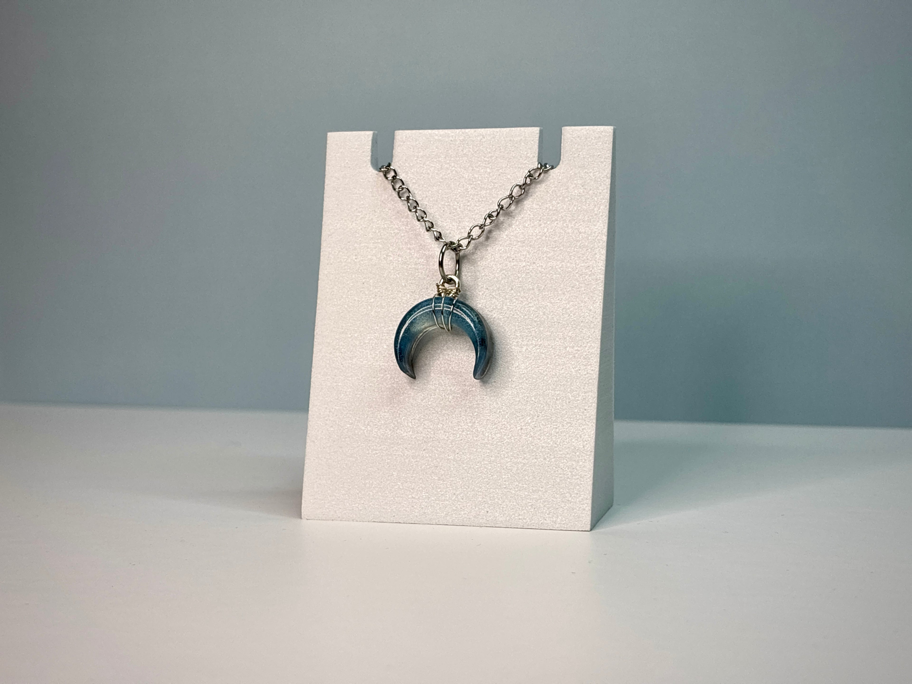 Necklace with a blue pendant on a white stand against a gray background