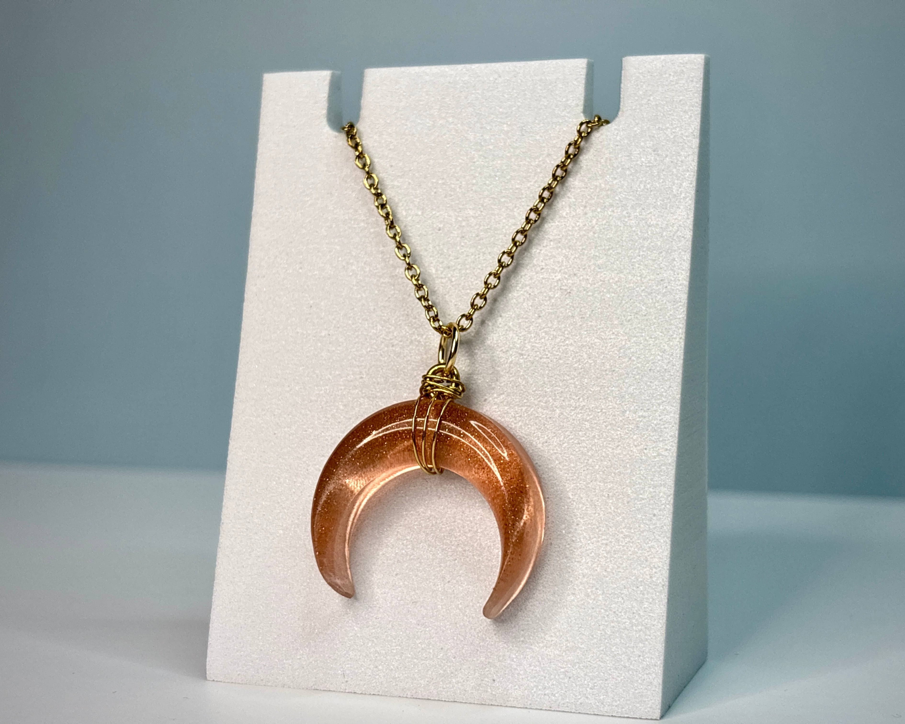 Bronze crescent moon pendant on a chain displayed on a white stand against a gray background