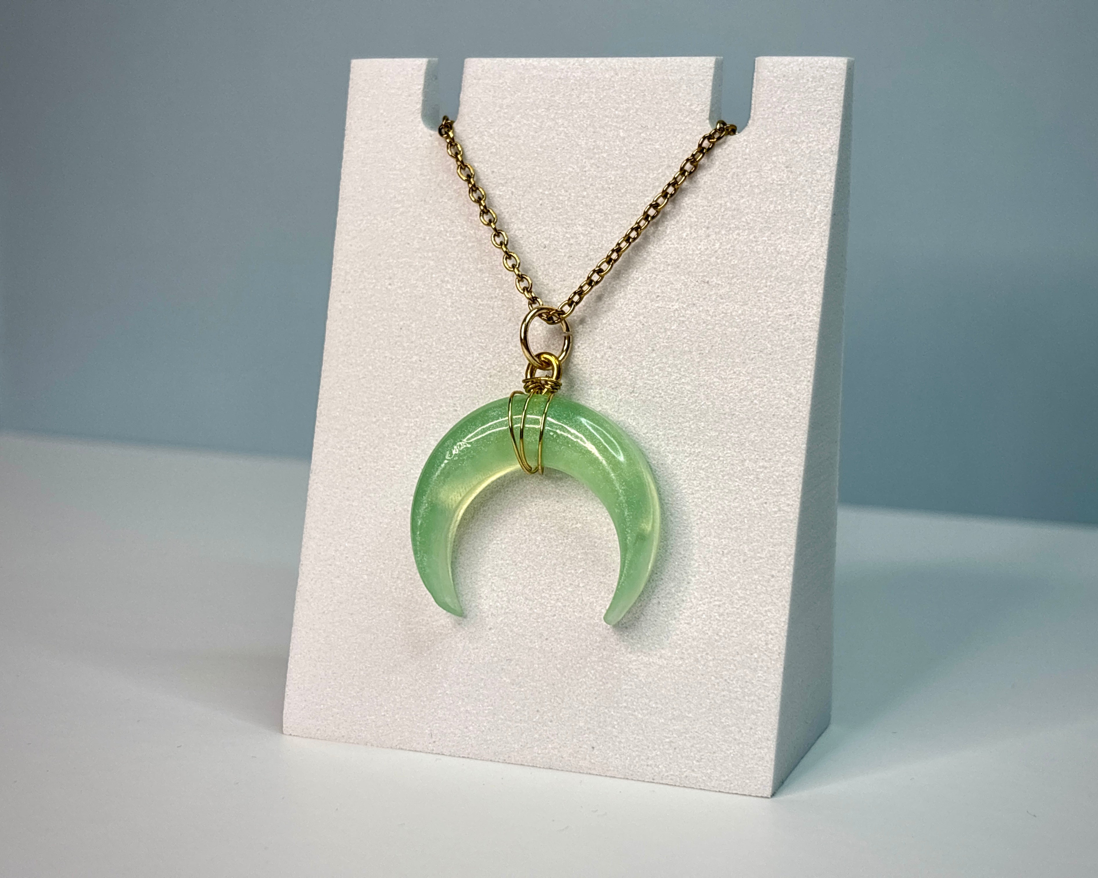 Green crescent moon necklace on a white stand with a gray background