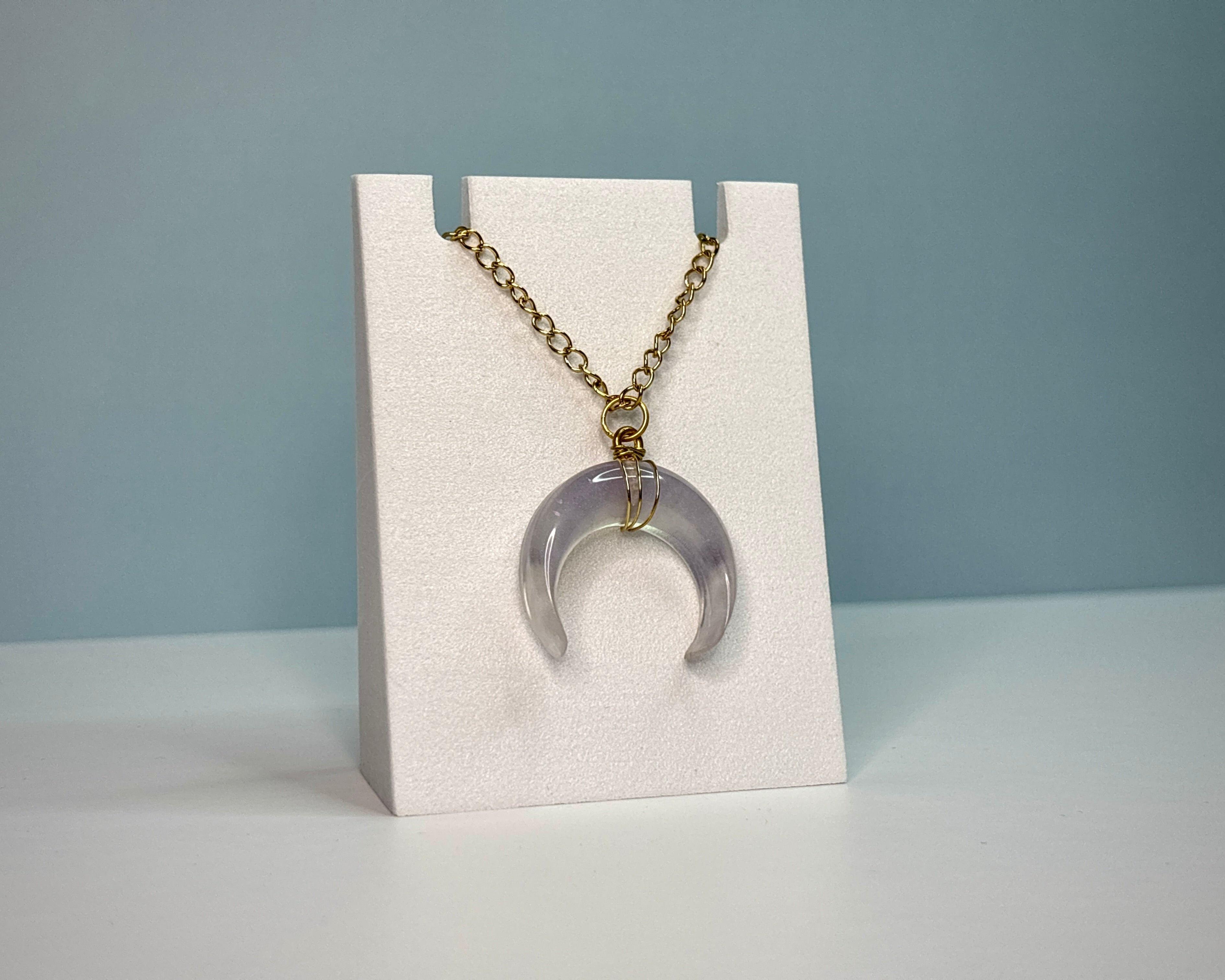 Necklace with a purple crescent moon pendant on a white stand against a gray background