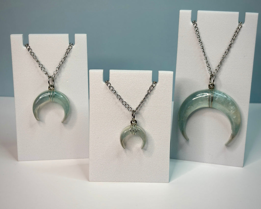 Three necklaces with crescent moon pendants on white stands against a gray background