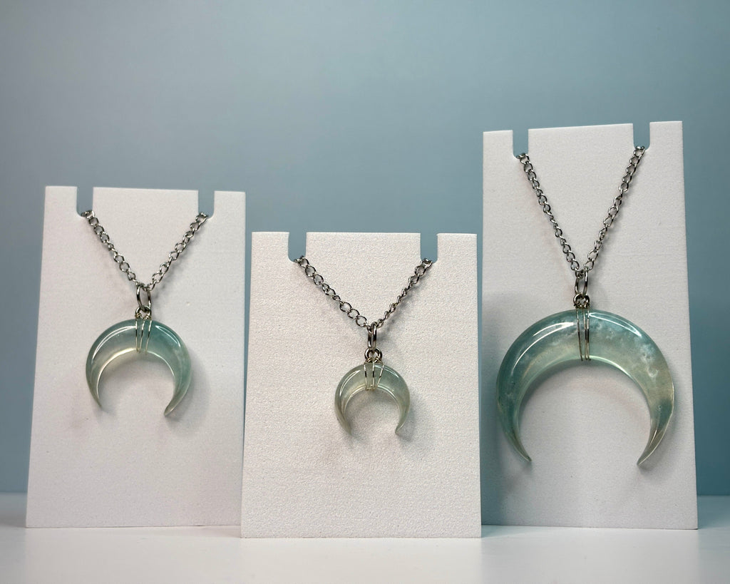 Three crescent moon-shaped pendants on white stands against a gray background