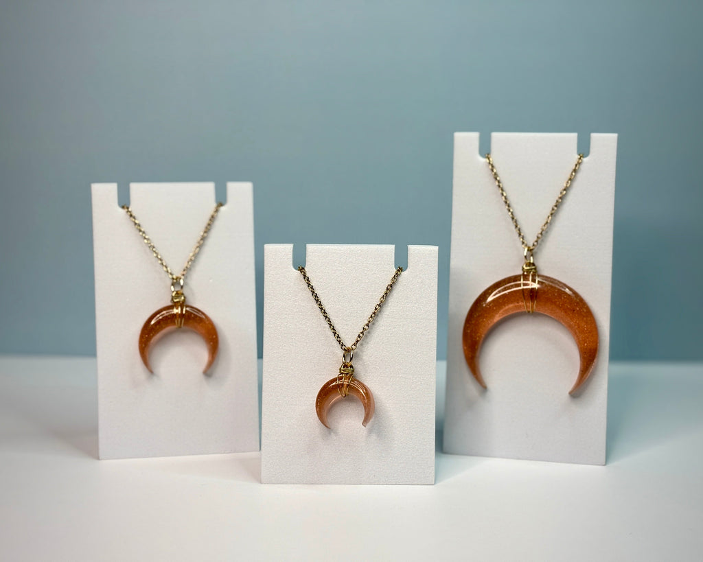 Three crescent moon-shaped pendants on white stands against a gray background
