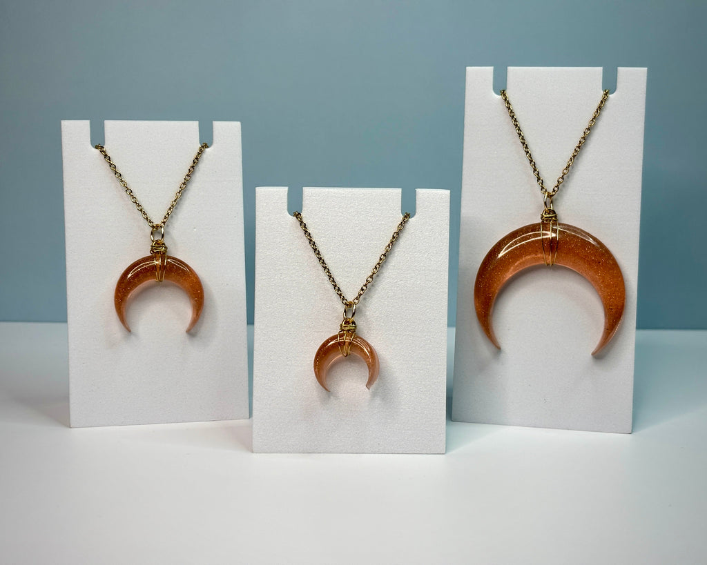 Three necklaces with crescent moon pendants on white stands against a gray background