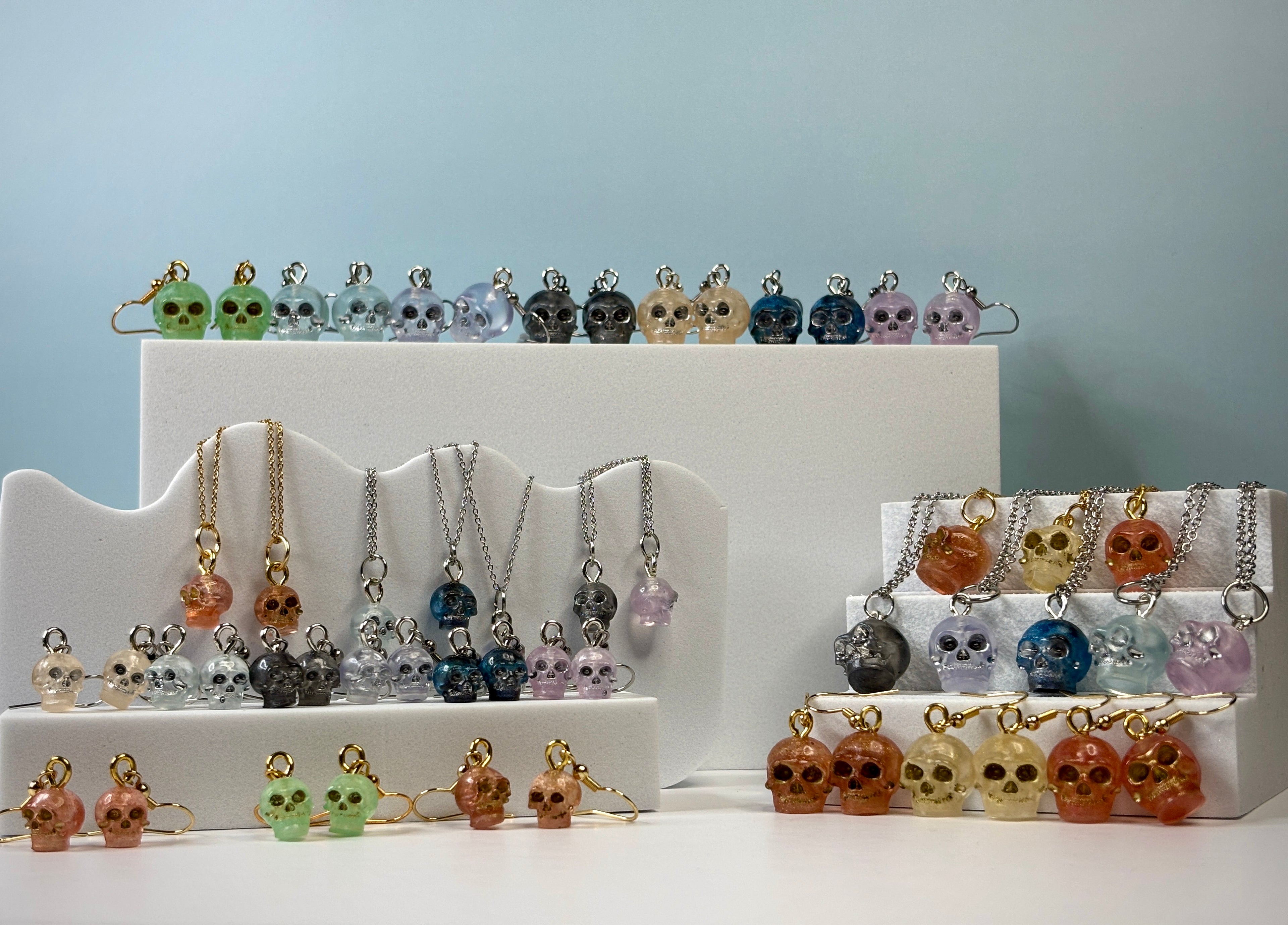 Assorted Skull Jewelry displayed on a white stand against a light blue background