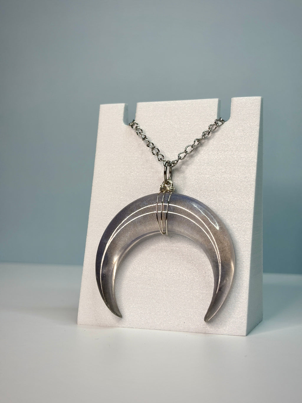 Silver crescent moon necklace on a white stand against a gray background