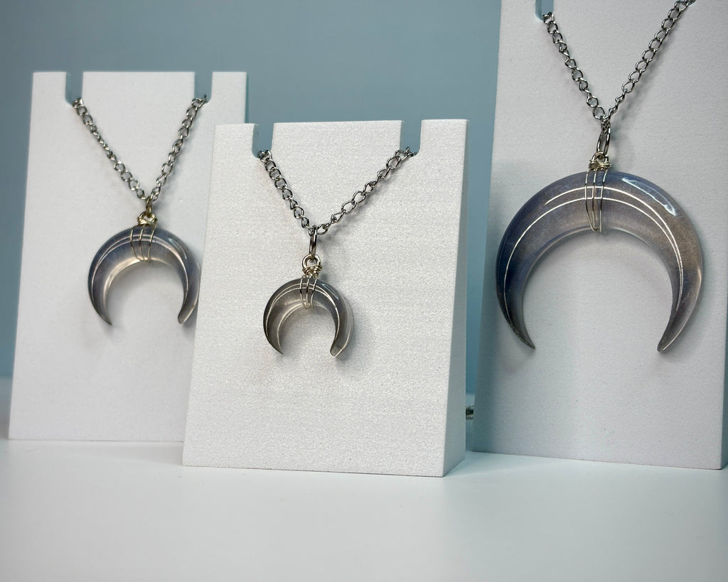 Silver crescent moon necklace on a white stand against a gray background