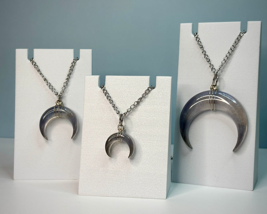 Crescent moon-shaped pendant necklaces on white stands against a gray background