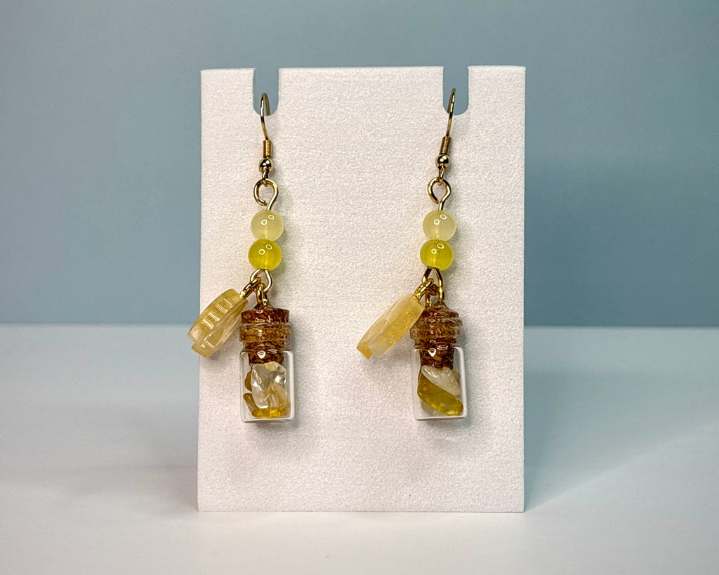 Pair of earrings with small bottles and beads on a white card against a blue background