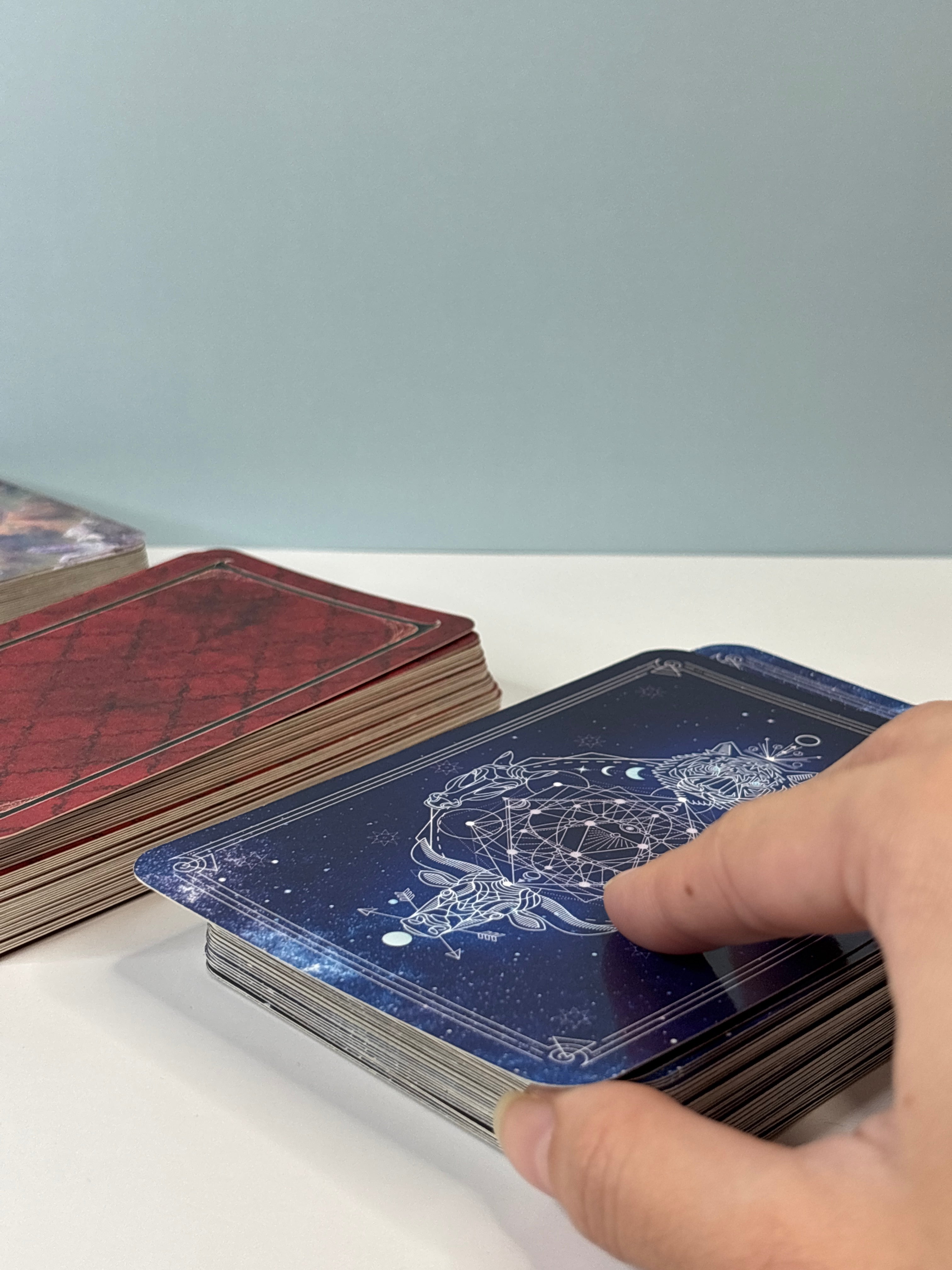 Hand holding a deck of cards with a blue card featuring a white design on a light gray background