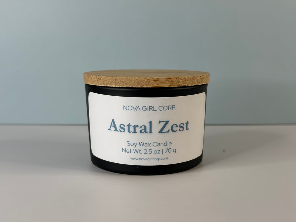 Astral Zest soy wax candle by Nova Girl Corp in a matte black jar with a bamboo lid, labeled with scent name and net weight 2.5 oz