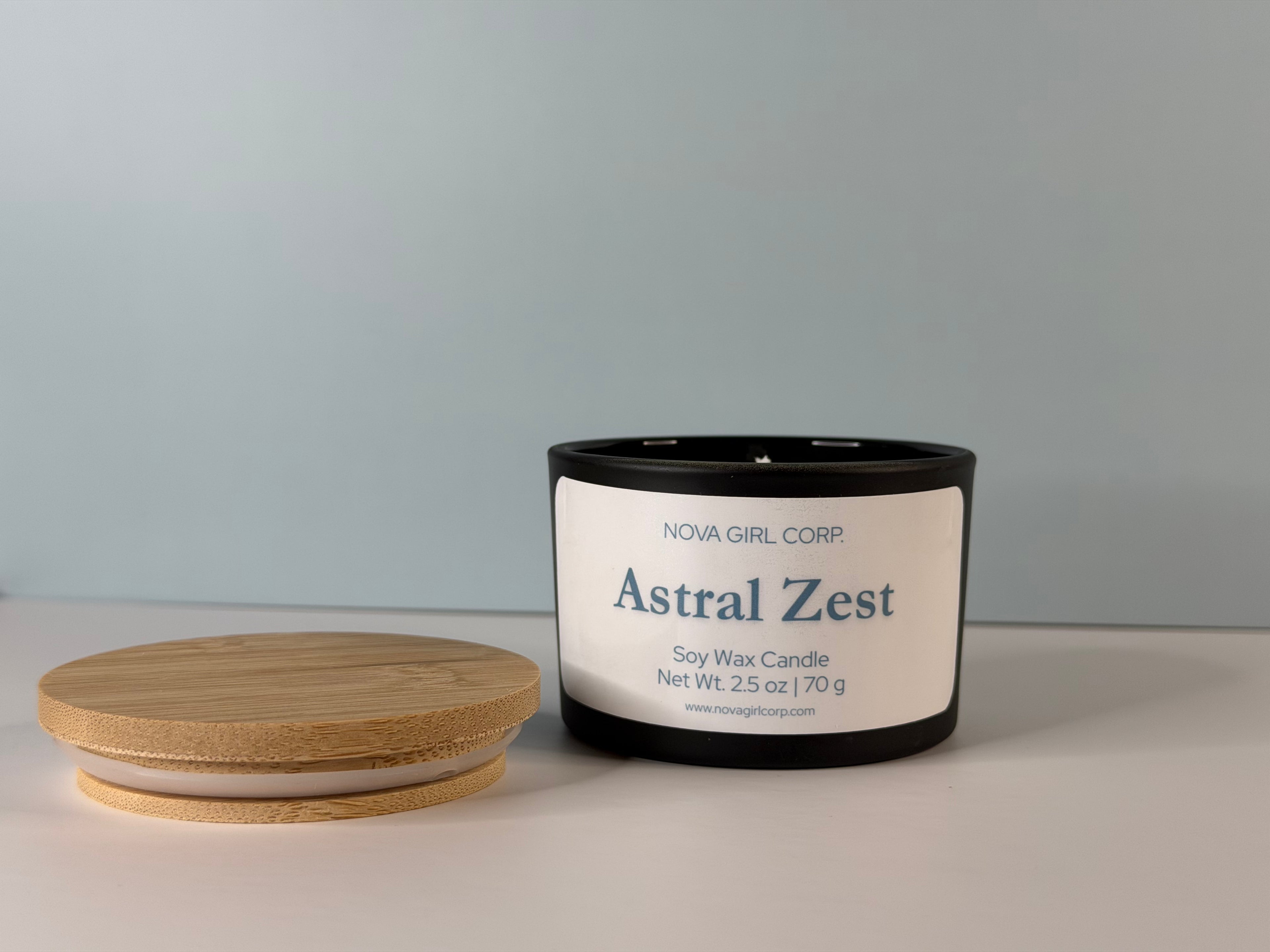 Astral Zest soy wax candle by Nova Girl Corp with bamboo lid removed, showing the natural soy wax surface and branded label, net weight 2.5 oz